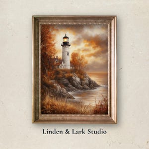 Puede incluir: Impresión artística enmarcada de un faro blanco y negro en una costa rocosa, rodeado de árboles otoñales. El cielo es dorado. Firmado "Linden & Lark Studio".