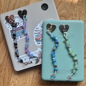 Op de afbeelding: Twee kralen boekenleggers met hartvormige clips. Eén boekenlegger heeft een mix van zwarte, grijze, paarse en blauwe kralen, terwijl de andere blauwe en groene kralen heeft. Beide hebben bedels, waaronder een walvis en een blad.
