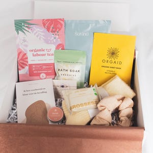 May include: A gift box filled with self-care items. The box contains a variety of products, including tea, bath soak, sheet mask, and a book. The packaging features a mix of colors, including pink, yellow, and green. The box is brown with white crinkle paper.