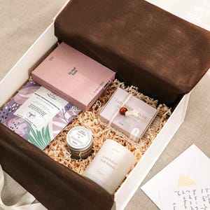 Pu&ograve; includere: Una scatola regalo bianca riempita di carta sminuzzata contenente una scatola rosa Herbal Bath, una bustina di t&egrave; viola e bianca, un vasetto di argilla per il viso, una candela bianca con etichetta A Moment for Mama, una scatola di lavanda e una nota.
