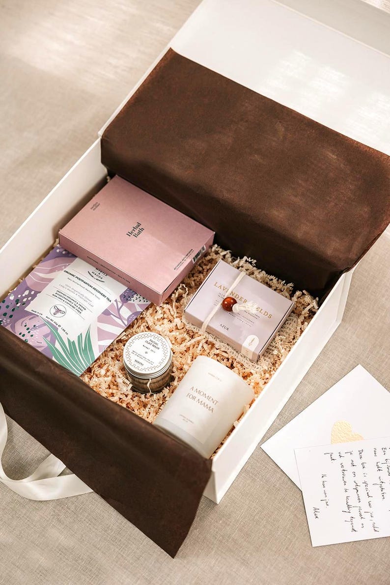 Pu&ograve; includere: Una scatola regalo bianca riempita di carta sminuzzata contenente una scatola rosa Herbal Bath, una bustina di t&egrave; viola e bianca, un vasetto di argilla per il viso, una candela bianca con etichetta A Moment for Mama, una scatola di lavanda e una nota.