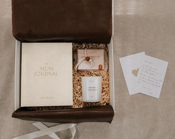 Può includere: Una confezione regalo contenente un diario color crema intitolato The Mum Journal, una piccola scatola rettangolare con l'etichetta Sunset Dreams, una candela bianca con l'etichetta A Moment for Mama e un biglietto scritto a mano con un cuore.