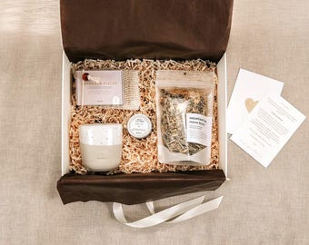 Può includere: Una confezione regalo contenente una saponetta Lavender Fields in una retina, una tazza in ceramica con finitura maculata, un piccolo barattolo rotondo e una bustina trasparente di Mountain Tea Mama Blend. Include due cartoline bianche con testo.