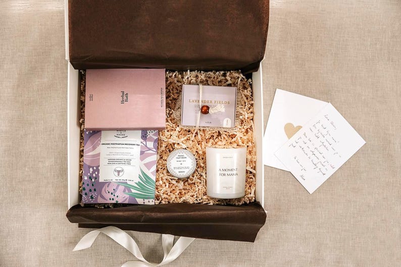 Pu&ograve; includere: Una scatola regalo riempita con carta sminuzzata contenente una scatola rosa Herbal Bath, un pacchetto Lavender Fields con una perlina rossa, un piccolo barattolo rotondo, una candela bianca con etichetta A Moment for Mama, una bustina di t&egrave; viola e un biglietto.