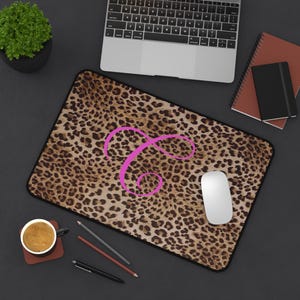 May include: A rectangular mousepad with a leopard print design and a large pink letter "P" in the center. The mousepad is on a dark surface with a computer, mouse, and other office supplies.