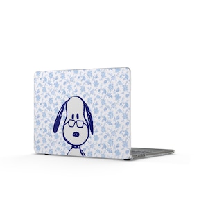 May include: Laptop with a blue and white floral pattern and a cartoon dog wearing glasses. The dog is drawn in navy blue. The laptop is open, displaying the design on the lid.
