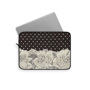 May include: A black laptop sleeve featuring a white polka dot pattern and a cream lace design. A silver laptop is partially inserted, highlighting the sleeve's decorative and protective qualities. The lace design is at the bottom.