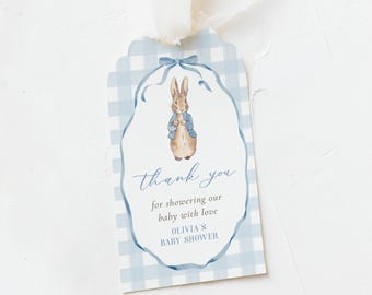 May include: A baby shower gift tag with a blue gingham pattern and a watercolor illustration of a rabbit wearing a blue jacket. The tag reads "thank you for showering our baby with love" and "Olivia's Baby Shower".