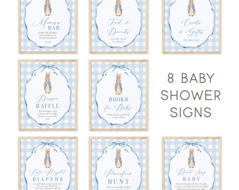 May include: Eight baby shower signs with a blue gingham background and a Peter Rabbit illustration. Each sign has a different message, including "Mimosa Bar," "Food & Drinks," and "Cards & Gifts."