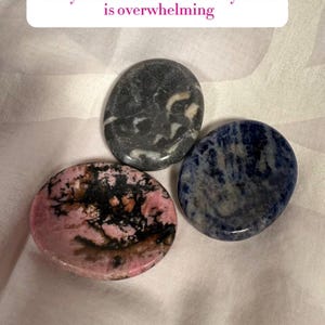May include: Three smooth worry stones in shades of pink, black, gray, and blue. The stones are oval-shaped and polished, with unique patterns and textures. Text on the image reads: Worry Stones for when anxiety/stress is overwhelming.