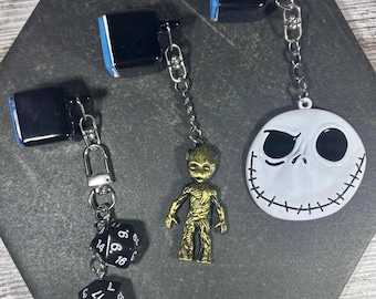 May include: Three black plastic clips with attached metal chains and charms. One clip features two black twenty-sided dice, one features a gold-toned metallic figure of a tree-like character, and one features a white circular face with black details.
