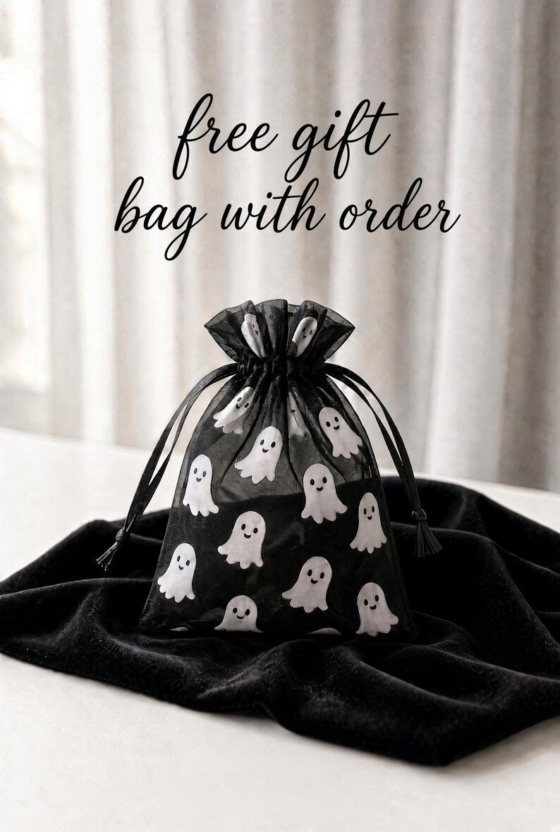 May include: A black sheer organza drawstring gift bag featuring a repeating pattern of small white ghosts with smiling faces. The text free gift bag with order is printed in black cursive script above the bag.