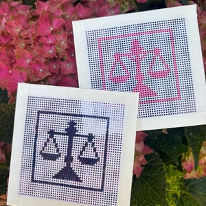 Puede incluir: Dos lienzos cuadrados de punto de aguja con un dise&ntilde;o de balanza de la justicia. Un lienzo muestra la balanza en hilo rosa vibrante, mientras que el otro lienzo presenta el mismo dise&ntilde;o de balanza bordado en hilo azul marino oscuro sobre malla blanca.