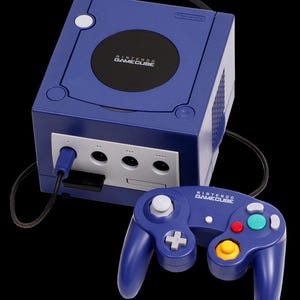 Pode incluir: Uma consola de videojogos Nintendo GameCube roxa com um comando roxo a condizer. A consola apresenta uma tampa de disco circular preta com o logótipo da Nintendo GameCube, um painel frontal branco com quatro portas e um cabo preto.