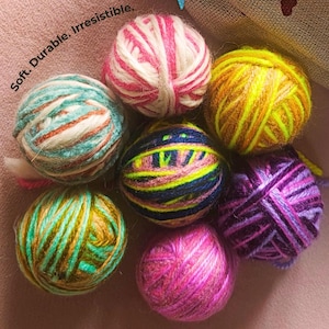 Könnte beinhalten: Eine Sammlung bunter Wollknäuel in verschiedenen Rosa-, Gelb-, Blau-, Grün- und Lilatönen. Die Wollknäuel sind fest gewickelt und kreisförmig angeordnet. Der Text "Soft. Durable. Irresistible." ist sichtbar.