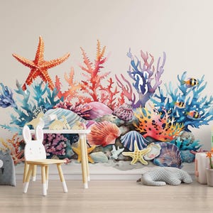 May include: A colorful watercolor mural of an underwater scene with coral, starfish, and fish. The mural is on a wall, with a small table and chair in front of it. Decorative items include stuffed animals and blocks.