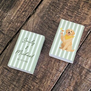 May include: Two small, rectangular boxes with a light green and white striped pattern. One box has the names "Emily & Michael" and the date "06.22.2026" printed on it. The other box features a cartoon golden retriever dog with a cocktail.