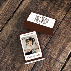 May include: Two brown boxes with white labels. One label reads "Dirty Thirty Club" in a script font. The other box has a photo of a child and the text "Jessica's 30th Vintage 1995". The boxes are on a wooden surface.