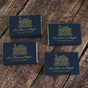 May include: Four navy blue boxes with a gold illustration of a house and the text "Our Place on Maple" and "THE SMITH FAMILY". The boxes are arranged on a wooden surface.