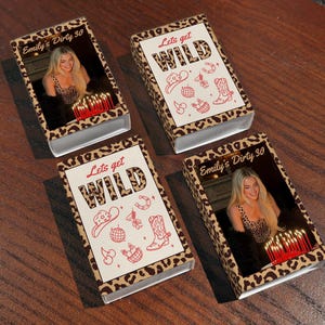 May include: Four matchbox sets with a leopard print design. Two boxes feature a photo with the text "Emily's Dirty 30". The other two boxes have the text "Lets get WILD" with cowboy-themed illustrations in red.