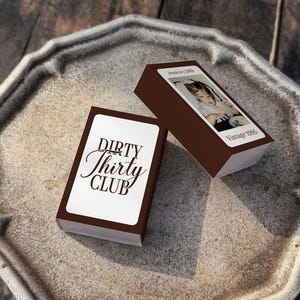 May include: Two brown boxes with white labels and text, one reading "DIRTY Thirty CLUB" in elegant script. The other box has a photo and the text "Jessica's 30th Vintage 1995". The boxes are on a decorative, octagonal, stone-colored tray.