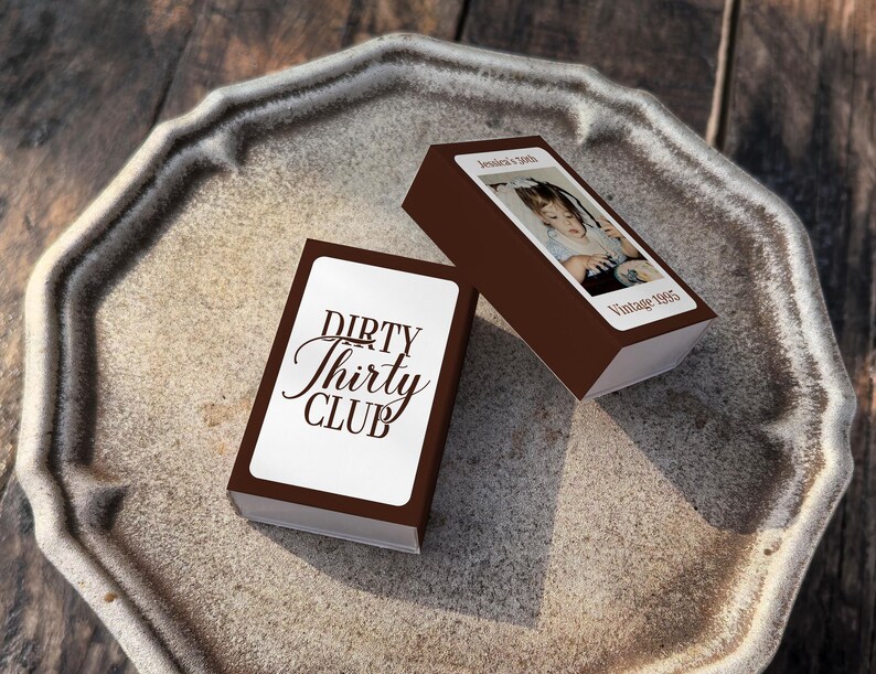 May include: Two brown boxes with white labels and text, one reading "DIRTY Thirty CLUB" in elegant script. The other box has a photo and the text "Jessica's 30th Vintage 1995". The boxes are on a decorative, octagonal, stone-colored tray.
