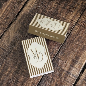 Peut inclure: Deux bo&icirc;tes d'allumettes rectangulaires avec un motif &agrave; rayures verticales marron et blanc. L'une affiche le texte Melody & Daniel avec la date et la phrase The perfect match. L'autre pr&eacute;sente une &eacute;tiquette festonn&eacute;e blanche avec les initiales MD.