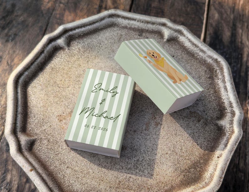 May include: Two small, light green striped boxes with the names "Emily & Michael" and the date "06.22.2026" printed on them. One box has a cartoon golden retriever wearing a yellow bandana. The boxes are on a decorative, octagonal plate.