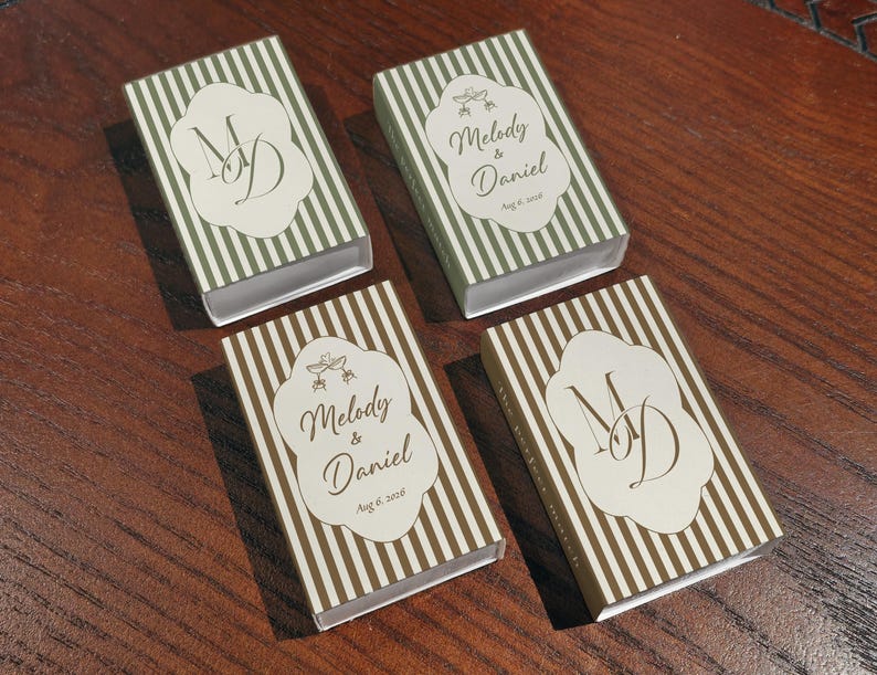Peut inclure: Quatre bo&icirc;tes d'allumettes rectangulaires avec un motif &agrave; rayures verticales vert olive et blanc. Deux bo&icirc;tes pr&eacute;sentent le monogramme MD, tandis que deux autres portent le texte Melody & Daniel avec la date Aug 6, 2026 et deux coupes de champagne.