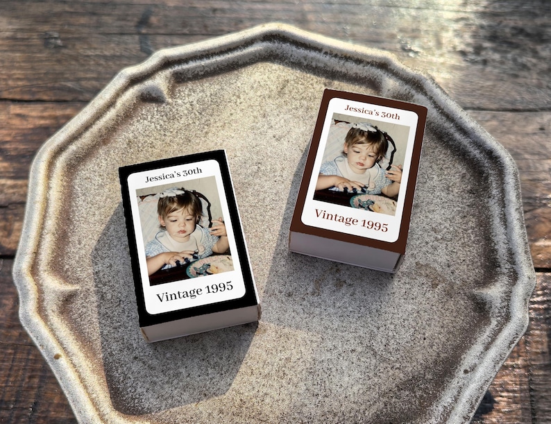 May include: Two rectangular boxes with a photograph of a young child. The boxes have the text "Jessica's 30th" and "Vintage 1995". One box is black, and the other is brown. The boxes are on a gray, textured tray.