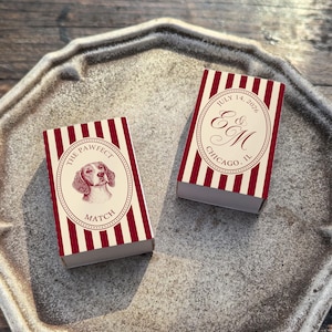 May include: Two matchboxes with red and white striped patterns. One box features a dog illustration and the text "THE PAWFECT MATCH". The other box has the text "July 14, 2026" and initials "E & M" with "CHICAGO, IL".