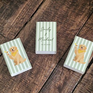May include: Three matchboxes with a light green and white striped pattern. Two boxes feature a golden retriever illustration holding a cocktail. The center box has the names "Emily & Michael" and the date "06.22.2026" in black script.
