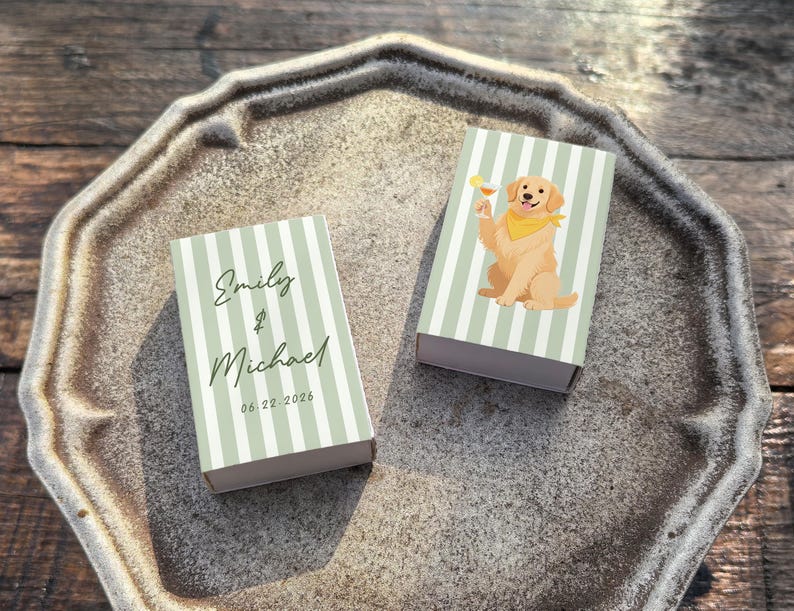 May include: Two matchboxes with a light green and white striped design. One box has the names "Emily & Michael" and the date "06.22.2026". The other box features a cartoon golden retriever dog holding a cocktail. The boxes are on a decorative tray.