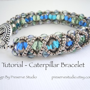 Puede incluir: Un brazalete de cuentas plateadas y azules con un cierre de palanca. El brazalete está hecho con pequeñas cuentas plateadas y cuentas más grandes azules, verdes y transparentes. El brazalete se llama "Caterpillar Bracelet" y es un diseño de Preserve Studio.