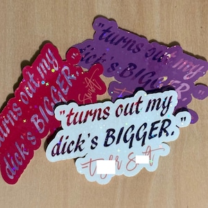 May include: A collection of glittery stickers in red, purple, and white, each featuring the phrase "turns out my dick's BIGGER." The stickers have a holographic effect and are arranged on a light brown surface.