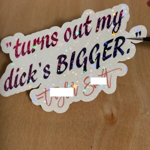 May include: A holographic sticker with the text "turns out my dick's BIGGER." The sticker has a white background with a scalloped edge and is decorated with small star-shaped sparkles. The text is in a mix of colors.