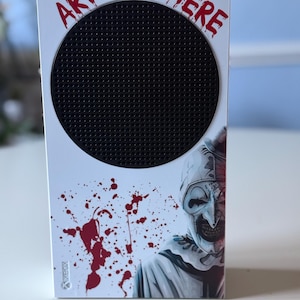 May include: White Xbox Series S console with a custom design featuring a black circular vent, the text "ART WAS HERE" in red, and a graphic of a scary clown with blood splatter.