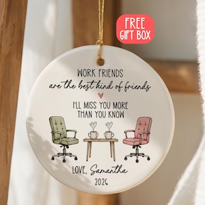 Puede incluir: Un adorno redondo de cerámica blanca colgado de un cordón dorado. El texto dice: WORK FRIENDS are the best kind of friends, I'LL MISS YOU MORE THAN YOU KNOW, LOVE, Samantha, 2026. Incluye una silla de oficina verde, una silla rosa y una mesa.