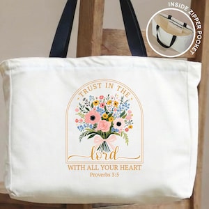 May include: White tote bag with black handles featuring a floral bouquet design and the text "Trust in the Lord with all your heart" from Proverbs 3:5. Includes an inside zipper pocket. The bouquet has pink, yellow, and blue flowers.