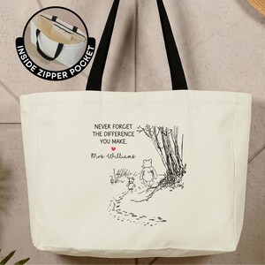 May include: A cream-colored canvas tote bag with black handles featuring a black line art illustration of Winnie the Pooh and Piglet walking. The text reads: NEVER FORGET THE DIFFERENCE YOU MAKE. Mrs. Williams. A small red heart and an inside zipper pocket.