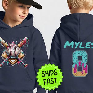Op de afbeelding: Marineblauwe hoodie met een honkbal- en gekruiste knuppels-ontwerp met een kleurrijk, druipend ontwerp. De achterkant van de hoodie toont de naam "Myles" en het nummer 8 ontworpen als een donut. De hoodie heeft een voorzak en een capuchon.