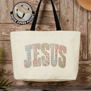 May include: A cream-colored canvas tote bag with black shoulder straps. The word JESUS is printed in large, block letters featuring a multi-colored floral and gingham patchwork pattern. A circular inset shows an interior zipper pocket.