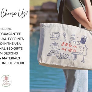 May include: A cream-colored canvas tote bag with black shoulder straps. The bag features a blue and red graphic print of sewing tools including a sewing machine, scissors, thimble, thread, iron, measuring tape, and dress form with the text I'll be in my office.