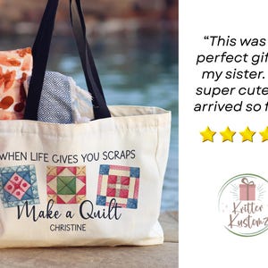Puede incluir: Un bolso de lona blanco con asas negras que presenta un gr&aacute;fico de tres bloques de edred&oacute;n coloridos y el texto "WHEN LIFE GIVES YOU SCRAPS Make a Quilt CHRISTINE". El bolso contiene una tela naranja estampada y un textil azul y blanco.