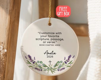 Può includere: Un ornamento rotondo in ceramica bianca appeso a un cordino dorato. Il testo recita: Customize with your favorite scripture, passage, or verse. BOOK CHAPTER: VERSE. Sotto sono presenti il nome Amelia, 2026, una piccola croce e rametti di lavanda.