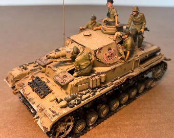 May include: A detailed model of a tan military tank with the number "432" in red on the side. Several miniature figures in olive green uniforms are positioned on the tank. The tank has visible tracks and a long barrel.