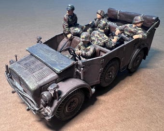 May include: A detailed model of a military vehicle with six soldiers in camouflage uniforms. The vehicle is painted in a dark brown color with visible details like the front grill, headlights, and wheels. The soldiers are seated inside the vehicle.