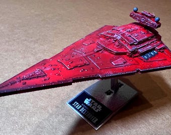 May include: A red Star Destroyer model from the Star Wars franchise. The model is a detailed replica of the iconic spaceship, with a triangular shape and intricate surface details. It is mounted on a stand with a Star Wars logo.