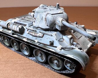 May include: A detailed model of a military tank, painted in shades of gray and white, with a weathered appearance. The tank features a long gun barrel, multiple wheels, and intricate detailing, suggesting a historical or collectible item.