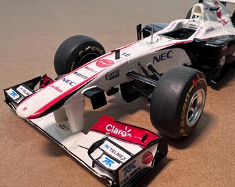 May include: A white and red Formula 1 race car model with black tires. The car has sponsor logos including "NEC", "Claro", and "Telmex". The number "16" is visible on the car's body.